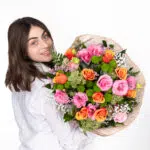 תמונה של דוגמנית מביטה מהצד ומחזיקה זר פרחים צבעוני אהבה בשדות ומחייכת