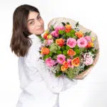 תמונה של דוגמנית עם חולצה לבנה מביטה מהצד ומחזיקה זר פרחים צבעוני אהבה בשדות